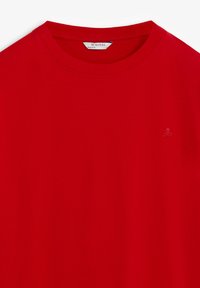 Rode crew neck t-shirt met een klein geborduurd doodskop en gekruiste beenderen logo op de linker borst en een Scalpers merklabel in de kraag.