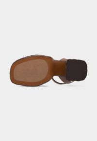 Κάτω όψη ενός καφέ δερμάτινου σανδαλιού με τετράγωνη μύτη και τακούνι μπλοκ σε λευκό φόντο.