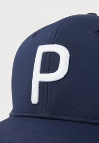 Casquette de baseball marine avec un design structuré, arborant une lettre "P" brodée en blanc sur le devant et un tissu texturé.