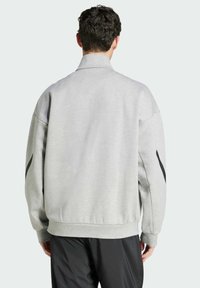 Grå överdimensionerad sweatshirt med hög krage, sänkt axelparti och svarta sidor. Tillverkad av mjukt material, med ribbade ärmslut och nederkant.