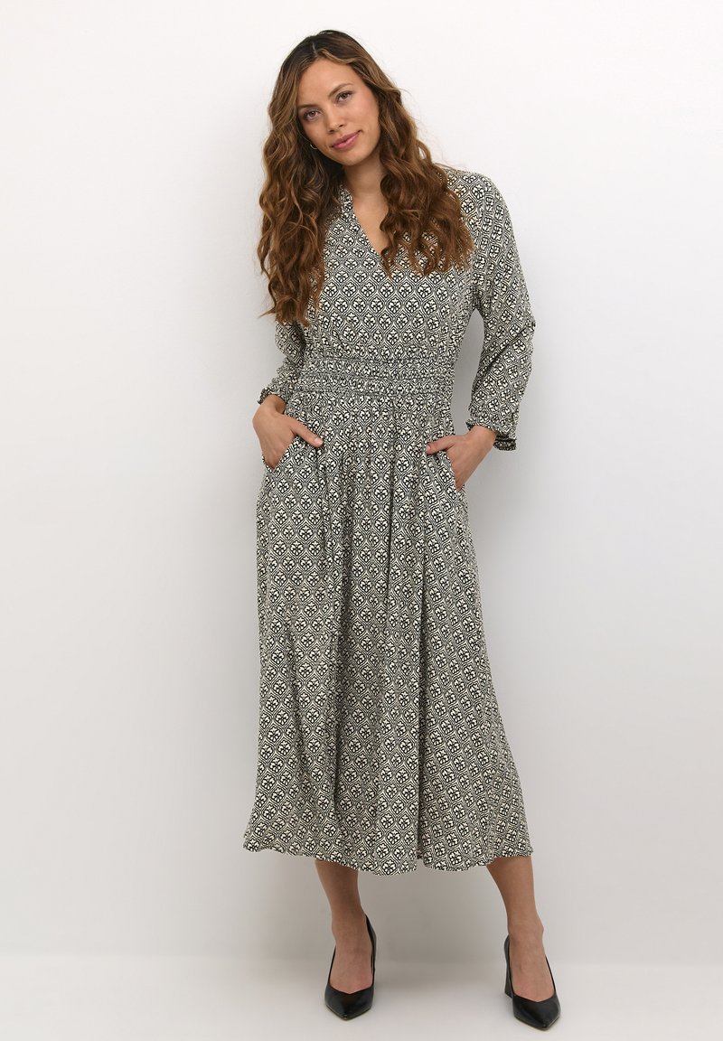 Maxi haljina u crnoj i bijeloj tkanini s uzorkom, s naglašenim strukom, dugim rukavima, V-izrezom i bočnim džepovima. Glatka tekstura.