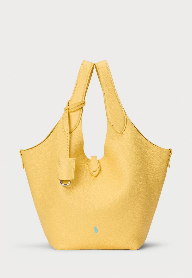 Žuta kožna torba s teksturiranim finišem, okrugli vrh, podesiva traka i mali dodatni džep, s turkiznim logotipom sprijeda.