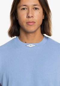 Jasnoniebieski sweter z okrągłym dekoltem w żebrowanym wzorze, z metką logo na dekolcie. Gładki materiał bez wzorów lub akcentów.