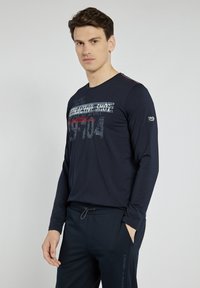 Niebieska koszulka z długim rękawem, wykonana z miękkiego materiału, z graficznym napisem w białym i czerwonym kolorze. Okrągły dekolt i slim fit. W połączeniu z pasującymi spodniami.