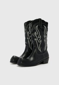 Botas de vaquero de cuero negro con bordado de llamas plateadas, puntera redondeada, tacón de altura media y costuras decorativas a lo largo de las costuras.