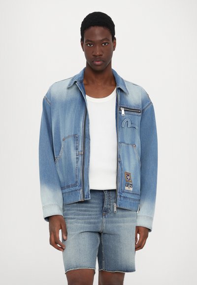Τζάκετ τζιν σε ανοιχτό μπλε χρώμα με ξεθωριασμένη υφή, δύο μπροστινές τσέπες, κλείσιμο με φερμουάρ και κεντημένο σχέδιο. Συνδυασμένο με αντίστοιχες τζιν βερμούδες.