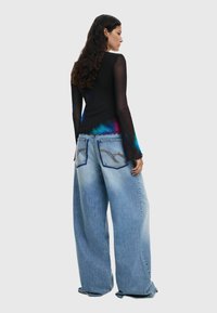 Bluza neagră cu mâneci lungi, accentuată cu un gradient colorat, asortată cu blugi oversized de culoare albastră deschis, cu o cusătură detaliată pe buzunarele din spate.