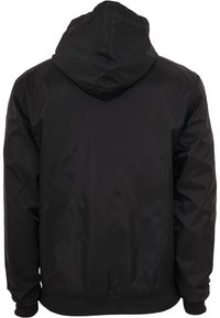 Veste à capuche noire à manches longues, poignets élastiques et taille ajustée, vue de dos sur fond blanc.