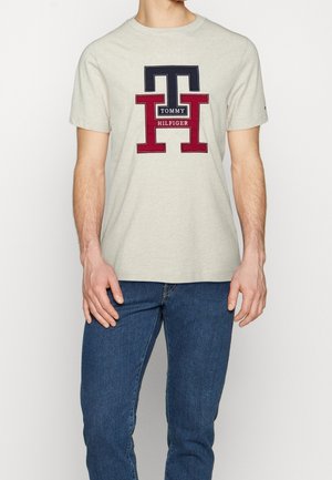 Kurze ärmelloses graues T-Shirt mit einem großen bestickten Logo in Marineblau und Bordeaux. Der Stoff ist weich und hat einen klassischen Rundhalsausschnitt.