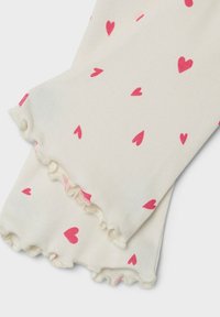 White leggings with pink heart pattern, featuring a ribbed texture and ruffled hem. The design includes scattered small hearts throughout.