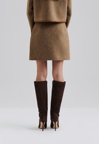 Gonna di lana marrone con un design a taglio dritto, abbinata a stivali di camoscio marrone scuro fino al ginocchio con tacchi a spillo e cerniere laterali.