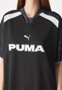 Czarny sportowy T-shirt z krótkim rękawem, z białym logo Puma i akcentami, żebrowanym dekoltem oraz teksturowanym wzorem materiału.