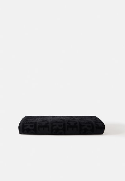 Serviette noire pliée avec un motif de lettres en relief, posée à plat sur une surface blanche.