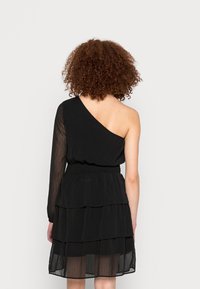 Vestido preto de um ombro só com uma manga longa transparente, saia em camadas com volantes e cintura elástica. Textura suave e design fluido.