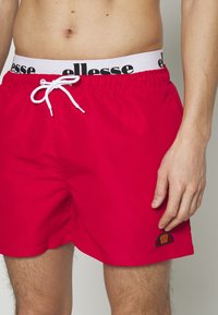 Rote Badewaren mit elastischem Bund und schwarzem Logo. Die Shorts haben einen Kordelzug und ein kleines gesticktes Logo am Saum.