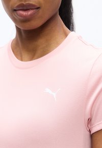 Κλείσιμο εικόνας ενός ατόμου που φοράει ροζ μπλούζα Puma με το λευκό λογότυπο Puma στο στήθος.