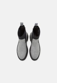 Harmaat mokkanahkaiset nilkkurit, joissa musta joustava sivupaneeli, pyöreä kärki ja teksturoitu kumipohja. Takana vetotakki.