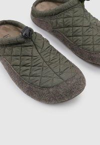 Zapatilla verde acolchada con suela suave de fieltro, con un detalle de lana gris en la zona de la punta y un cordón ajustable para un mejor ajuste.