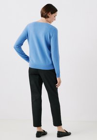 Maglione azzurro chiaro, aderente, realizzato in morbido tessuto a maglia, abbinato a pantaloni neri a sigaretta e ballerine nere. La vista posteriore evidenzia il design semplice del maglione.