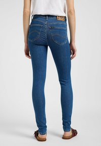Jeans ajustados azul con una alta cintura, que cuentan con bolsillos traseros y un parche de cuero en la cintura. La tela tiene una textura suave y elástica.