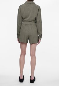 Olivově zelený krátký overal s límečkem, dlouhými rukávy, elastickým pasem a měkkou texturou, opatřený knoflíkovými detaily na manžetách.