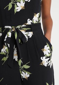 Robe en tissu noir avec un motif floral blanc et des feuilles vertes. Comprend une ceinture à nouer à la taille et des poches latérales. Texture douce.
