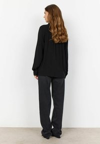 Camisa negra de manga larga, ajuste holgado, detalle plisado en la parte trasera, combinada con pantalones de pierna ancha gris oscuro, tela suave, diseño minimalista.
