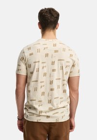 Cremfarbendes T-Shirt mit kurzen Ärmeln und einem strukturierten, gemusterten Design in Braun. Rundhalsausschnitt und schmale Passform, geeignet für die Freizeit.
