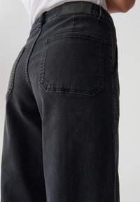Pantaloni in denim nero con un design a gamba dritta, dotati di tasche posteriori, una finitura in tessuto testurizzato e un accentuato punto vita testurizzato.