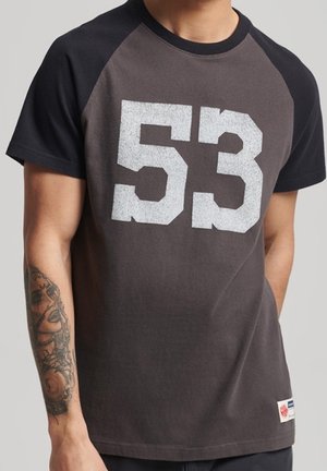 Graues Baumwoll-T-Shirt mit schwarzen Raglanärmeln, auf der Vorderseite mit der weißen, fetten Nummer "53" bedruckt und einem kleinen Etikett am Saum.