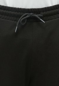 Fekete melegítőnadrág derékrészének közelképe, ahol húzózsinór van, rugalmas, bordázott szalaggal és texturált anyaggal.