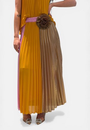 Donna che indossa una gonna plissettata in senape, taupe e rosa con una cintura decorativa a fiore grande e décolleté con punta impreziosita.