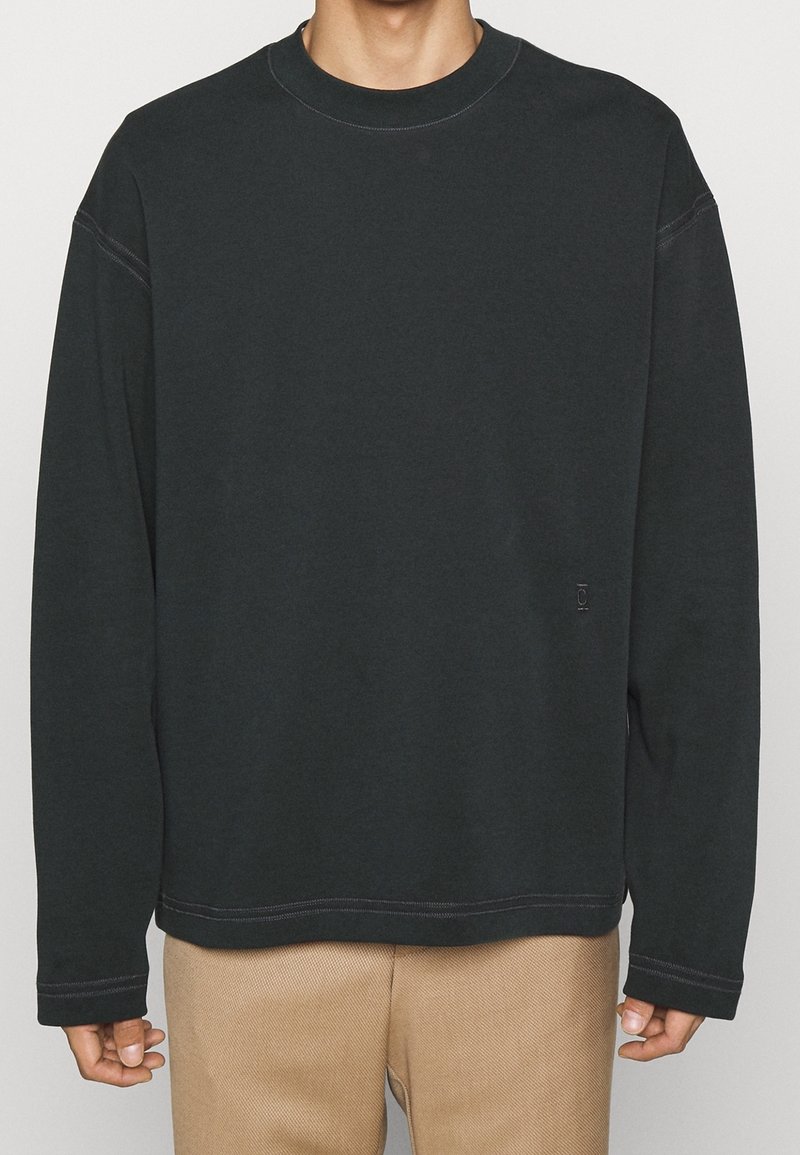 Sweatshirt gris foncé avec un col rond, des manches longues et des détails de couture visibles. Fabriqué en tissu doux avec une coupe décontractée.