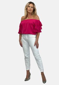 Jasnoróżowa bluzka na ramiączkach z falbanami, w połączeniu z białymi dopasowanymi spodniami i wysokimi obcasami w wzór w węża.