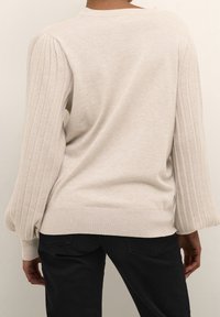 Beige Pullover mit gerippten Ärmeln und einem runden Ausschnitt, strukturierter Stoff, lässige Passform und einem etwas längeren Rückensaum.