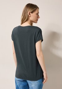 Camiseta de manga corta gris oscuro con un ajuste relajado, textura suave y dobladillo trasero redondeado, combinada con jeans de color azul claro.