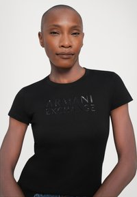 Black cotton t-shirt featuring a fitted design and short sleeves, with a glossy embossed logo reading "ARMANI EXCHANGE" across the front.