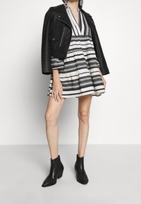 Svart skinnjacka över en randig klänning med vita och svarta horisontella ränder, med volanger vid fållen. Svarta ankelstövlar.