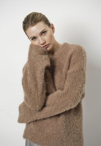 Lichtbruin gebreid sweater van pluizig materiaal, met lange mouwen en een losse pasvorm, een brede halslijn en een zachte textuur.