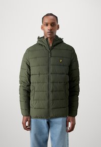 Veste rembourrée verte avec fermeture éclair à l'avant et capuche. Présente une texture matelassée verticale et un petit logo jaune sur la poitrine gauche.