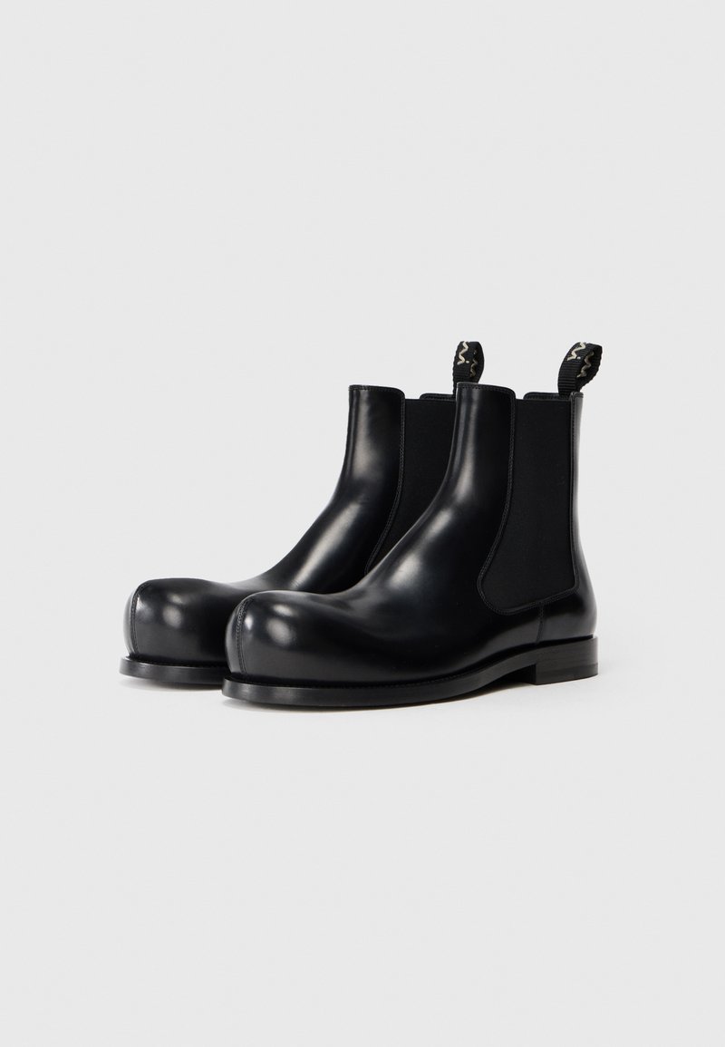 Sorte læder Chelsea støvler med elastiske indlæg, afrundet tå og teksturerede pull tabs. Flad gummisål, glat overflade, minimalistisk design.