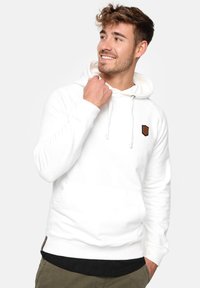Sudadera blanca de algodón con cordones, bolsillo frontal y un pequeño parche de logo marrón en el pecho. Textura suave y corte regular.