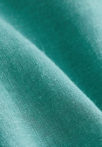 Gros plan sur un tissu tissé bleu sarcelle montrant la texture détaillée et les plis, avec un éclairage doux mettant en valeur la surface du matériau.