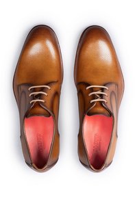 Braune Lederdressschuhe mit Durchbruchsdesign, passenden Schnürsenkeln, roten Einlegesohlen und kontrastierenden dunkleren Akzenten um die Öffnungen.