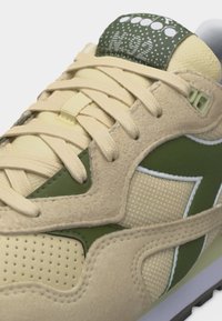 Κοντινό πλάνο μπεζ και πράσινου αθλητικού παπουτσιού με υφή ύφασμα, επενδύσεις από σουέτ, μπεζ κορδόνια και λεπτομέρεια με μοτίβο στη γλώσσα.