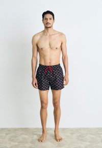 Pantaloni de înot cu un fundal negru, având un model repetat de logo-uri în roșu și alb. Talie cu șnur, materialul este ușor și neted.