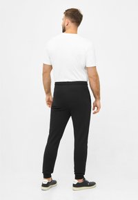 Schwarze Sweatpants mit elastischem Bund, schmalem Schnitt und gerippten Bündchen, kombiniert mit einem schlichten weißen T-Shirt und schwarzen Turnschuhen.