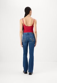 Punane hästi istuv lõhikuga tank top õhukeste rihmadega ja sinised laiad teksad, millel on eriline tasku tikand ja beež nahkpadi vöökoha juures.