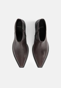 Bottines en cuir brun foncé avec bouts pointus, fermetures éclair latérales et semelles noires vues de dessus sur un fond uni.