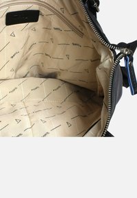 Den svarta axelväskans inredning har en tan-färgad foder med ett geometriskt mönster. Inkluderar en zippered ficka och ett rymligt huvudfack.
